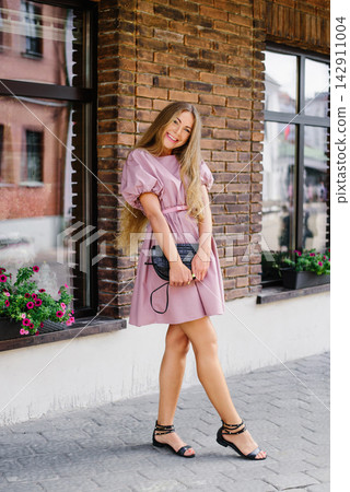 Joyful woman in pink summer dress reaching forward on city street Joyful woman in pink summer dress reaching forward on city street 142911004