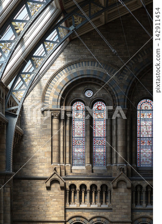 Sunlight streams through the arched windows of a building, creating distinct patterns of light and shadow on the detailed stonework walls, arched windows and stained-glass. Sunlight streams through the arched windows of a building, creating distinct patterns of light and shadow on the detailed stonework walls, arched windows and stained-glass. 142911454