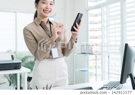 Young Businesswoman Working at Office Desk While Managing Documents and Mobile Communication. Young Businesswoman Working at Office Desk While Managing Documents and Mobile Communication. 142911577