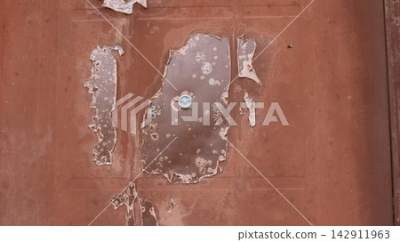 Delamination of the polymer coating on a metal door. Around the peephole, the paint has cracked, bubbled, and peeled off in large flakes. An example of material corrosion and wear. Delamination of the polymer coating on a metal door. Around the peephole, the paint has cracked, bubbled, and peeled off in large flakes. An example of material corrosion and wear. 142911963