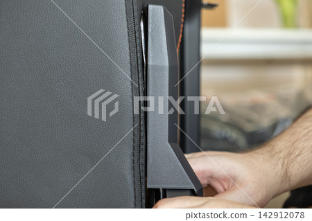 A hand secures a plastic cover onto the side of a leather gaming chair frame, detailing the assembly process of professional ergonomic furniture in a clean home workspace setting today A hand secures a plastic cover onto the side of a leather gaming chair frame, detailing the assembly process of professional ergonomic furniture in a clean home workspace setting today 142912078