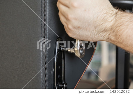 A hand uses a ratchet wrench to fasten a metal bolt into a black gaming chair frame, symbolizing assembly work during home office furniture setup and DIY interior equipment repair A hand uses a ratchet wrench to fasten a metal bolt into a black gaming chair frame, symbolizing assembly work during home office furniture setup and DIY interior equipment repair 142912082