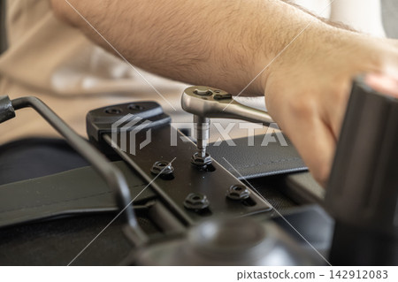 A person tightens a bolt on an office chair using a metal ratchet wrench, showcasing assembly, home repair, DIY furniture maintenance, and professional equipment setup for workspaces A person tightens a bolt on an office chair using a metal ratchet wrench, showcasing assembly, home repair, DIY furniture maintenance, and professional equipment setup for workspaces 142912083
