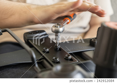 A hand uses a ratchet tool to tighten a bolt on a black office chair frame, demonstrating professional furniture assembly and maintenance in a residential interior design workspace A hand uses a ratchet tool to tighten a bolt on a black office chair frame, demonstrating professional furniture assembly and maintenance in a residential interior design workspace 142912084