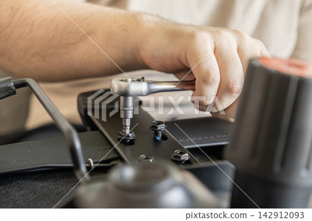 A hand uses a ratchet tool to tighten a metal bolt on office chair furniture, representing home assembly, DIY maintenance, repair tasks, and professional workspace construction projects A hand uses a ratchet tool to tighten a metal bolt on office chair furniture, representing home assembly, DIY maintenance, repair tasks, and professional workspace construction projects 142912093