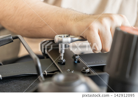 A hand tightens a bolt on an office chair using a metal ratchet wrench, showcasing assembly, repair, or maintenance tasks in a professional workspace setting for home or business usage A hand tightens a bolt on an office chair using a metal ratchet wrench, showcasing assembly, repair, or maintenance tasks in a professional workspace setting for home or business usage 142912095