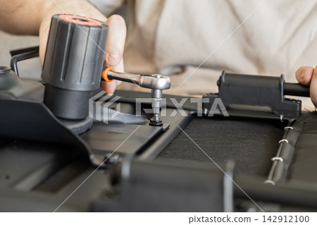 A person tightens a screw with a ratchet on a black office chair base during home furniture assembly, illustrating DIY improvement and repair work in a modern living environment setup A person tightens a screw with a ratchet on a black office chair base during home furniture assembly, illustrating DIY improvement and repair work in a modern living environment setup 142912100