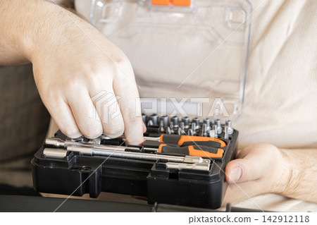 A hand selecting a socket wrench from a compact professional toolkit box, representing precision maintenance, automotive repair, and DIY craftsmanship in a home improvement project set A hand selecting a socket wrench from a compact professional toolkit box, representing precision maintenance, automotive repair, and DIY craftsmanship in a home improvement project set 142912118
