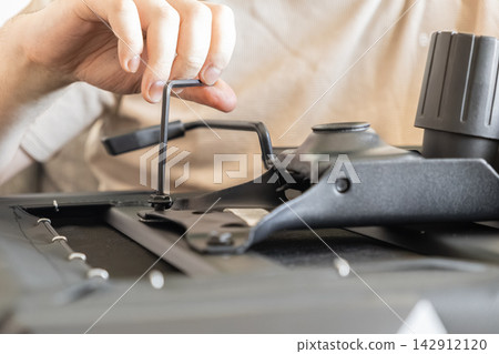 A person tightens a screw with an allen wrench to assemble a modern office chair, illustrating self-service furniture installation and maintenance in a professional workplace A person tightens a screw with an allen wrench to assemble a modern office chair, illustrating self-service furniture installation and maintenance in a professional workplace 142912120