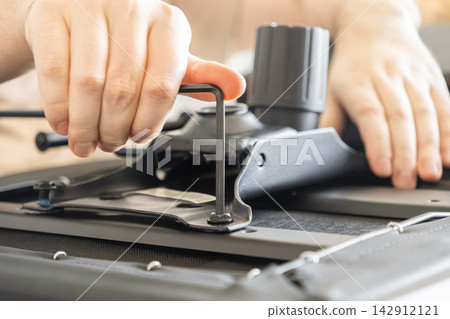 A person uses an Allen wrench to tighten a bolt on a black office chair mechanism, illustrating furniture assembly, DIY home improvement, and professional maintenance work tasks A person uses an Allen wrench to tighten a bolt on a black office chair mechanism, illustrating furniture assembly, DIY home improvement, and professional maintenance work tasks 142912121