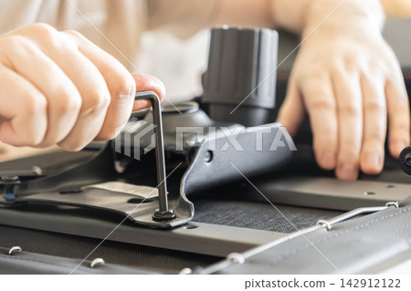 A person tightens a bolt with an allen key while assembling a modern office chair at home, representing DIY furniture construction, home improvement, and manual technical assembly tasks A person tightens a bolt with an allen key while assembling a modern office chair at home, representing DIY furniture construction, home improvement, and manual technical assembly tasks 142912122