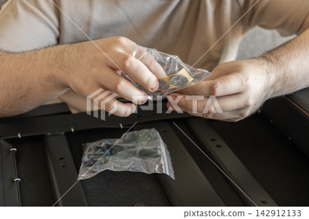 A person assembling furniture by opening a small bag containing adhesive felt pads, demonstrating the careful process of preparing hardware for home improvement and product installation A person assembling furniture by opening a small bag containing adhesive felt pads, demonstrating the careful process of preparing hardware for home improvement and product installation 142912133