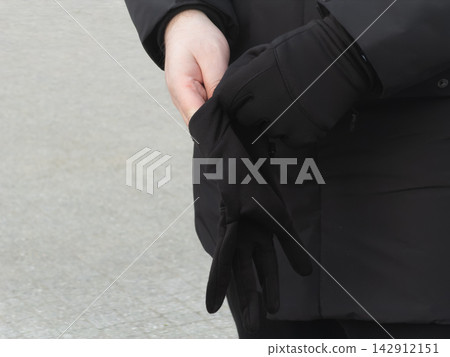 A person pulls on warm black winter gloves outdoors, preparing for cold weather by protecting hands from icy temperatures while wearing a thick jacket in a seasonal outdoor setting A person pulls on warm black winter gloves outdoors, preparing for cold weather by protecting hands from icy temperatures while wearing a thick jacket in a seasonal outdoor setting 142912151