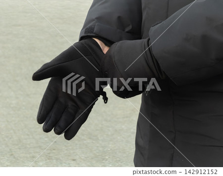 A person wears black winter gloves with a matching down jacket, ready for cold weather outdoor activities, emphasizing comfort, protection, and warmth during a chilly climate A person wears black winter gloves with a matching down jacket, ready for cold weather outdoor activities, emphasizing comfort, protection, and warmth during a chilly climate 142912152