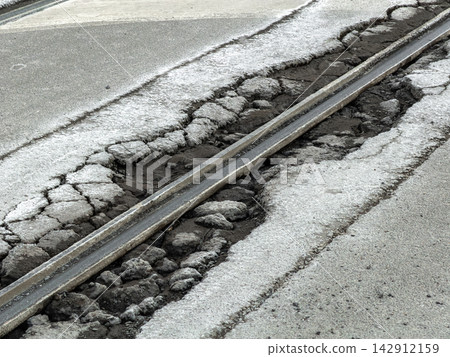A damaged asphalt road surface surrounding a rusty tram rail creates a hazardous street scene, highlighting infrastructure decay and the urgent need for city maintenance and repair work A damaged asphalt road surface surrounding a rusty tram rail creates a hazardous street scene, highlighting infrastructure decay and the urgent need for city maintenance and repair work 142912159