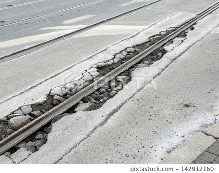 A damaged tram track embedded in broken asphalt road pavement shows crumbling concrete and debris along the rail, highlighting urban decay, infrastructure neglect and hazardous transit A damaged tram track embedded in broken asphalt road pavement shows crumbling concrete and debris along the rail, highlighting urban decay, infrastructure neglect and hazardous transit 142912160