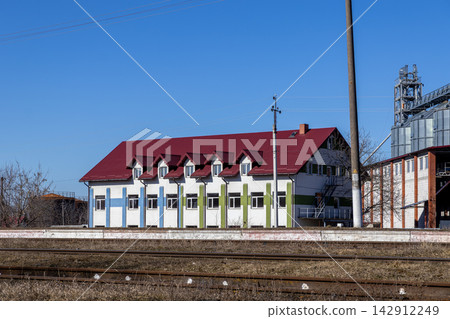 A modern white industrial office building with a red roof stands beside railway tracks under a clear blue sky, representing efficient logistics, agricultural trade, and infrastructure 142912249