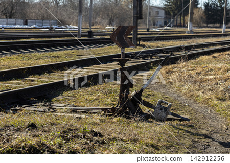 A vintage manual railway switch mechanism stands beside metal tracks, serving as an essential control point for navigating trains through the complex network of a historic station yard A vintage manual railway switch mechanism stands beside metal tracks, serving as an essential control point for navigating trains through the complex network of a historic station yard 142912256