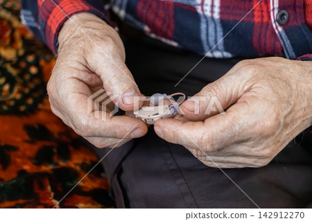 A senior person carefully holding a small modern hearing aid device to highlight professional healthcare support and effective accessibility solutions for improved daily living A senior person carefully holding a small modern hearing aid device to highlight professional healthcare support and effective accessibility solutions for improved daily living 142912270