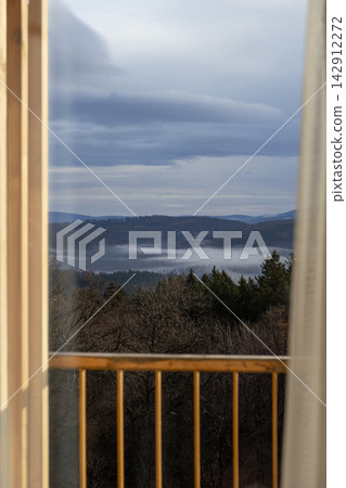 A view of the misty morning forest from a wooden balcony, showcasing nature landscape beauty and the tranquil atmosphere of a remote mountain retreat perfect for travel marketing 142912272