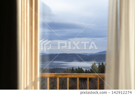 A view of pine forest mountains and morning mist through a bedroom window, conveying tranquil solitude, natural beauty, and a cozy escape in a quiet mountain cabin resort stay A view of pine forest mountains and morning mist through a bedroom window, conveying tranquil solitude, natural beauty, and a cozy escape in a quiet mountain cabin resort stay 142912274