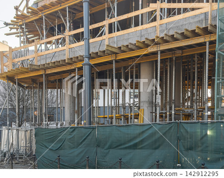 A building structure under construction with metal scaffolding and wooden supports, reflecting urban development, architectural progress, and the industrial growth of a modern city A building structure under construction with metal scaffolding and wooden supports, reflecting urban development, architectural progress, and the industrial growth of a modern city 142912295