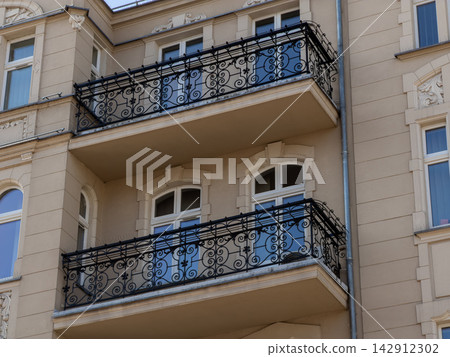 An ornate iron balcony railing on a beige residential building facade, highlighting classical architectural design and heritage urban style in a peaceful European neighborhood setting An ornate iron balcony railing on a beige residential building facade, highlighting classical architectural design and heritage urban style in a peaceful European neighborhood setting 142912302