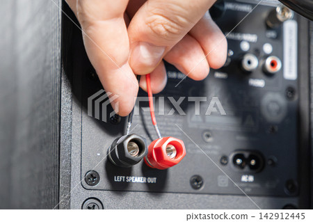 A person connects red and black audio wires into terminals of a sound speaker, showcasing technical setup, precise installation, and quality home theater maintenance for stereo systems A person connects red and black audio wires into terminals of a sound speaker, showcasing technical setup, precise installation, and quality home theater maintenance for stereo systems 142912445