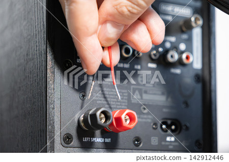 A hand holding stripped speaker wires ready to connect to red and black binding post terminals on an audio device, illustrating home theater installation and professional repair work A hand holding stripped speaker wires ready to connect to red and black binding post terminals on an audio device, illustrating home theater installation and professional repair work 142912446