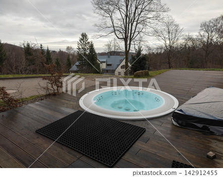 A circular hot tub installed on a rustic wooden deck overlooking a serene forest landscape, providing a luxurious outdoor spa experience for relaxation in a tranquil countryside setting A circular hot tub installed on a rustic wooden deck overlooking a serene forest landscape, providing a luxurious outdoor spa experience for relaxation in a tranquil countryside setting 142912455