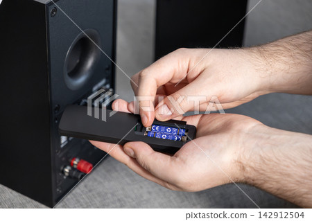 A hand placing alkaline batteries into a remote control for a home audio speaker system, representing equipment maintenance and power management for modern electronic device set up 142912504