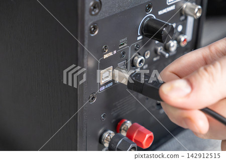 A hand plugging a cable into a professional speaker back panel for digital audio connection, depicting the setup process for high quality sound equipment in a modern home studio system A hand plugging a cable into a professional speaker back panel for digital audio connection, depicting the setup process for high quality sound equipment in a modern home studio system 142912515