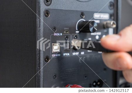 A hand plugging a cable into the rear panel of a professional audio speaker for digital connectivity, highlighting technical setup and home entertainment sound system installation work A hand plugging a cable into the rear panel of a professional audio speaker for digital connectivity, highlighting technical setup and home entertainment sound system installation work 142912517