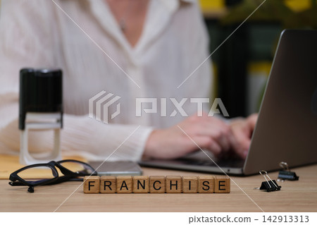 Business professional engaged in franchise planning while typing on a laptop at a wooden desk Business professional engaged in franchise planning while typing on a laptop at a wooden desk 142913313