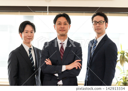Three men in suits stand with their arms crossed and look at the camera. Three men in suits stand with their arms crossed and look at the camera. 142913334
