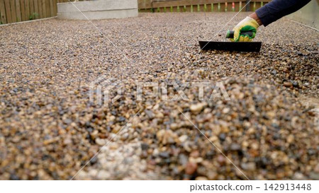 Construction worker laying a resin bound gravel patio floor with a trowel, closeup on hand Construction worker laying a resin bound gravel patio floor with a trowel, closeup on hand 142913448