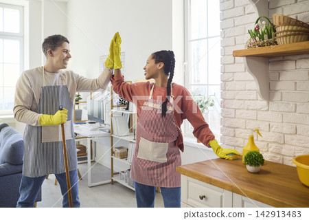 Smiling couple high five during kitchen cleaning, teamwork, motivation and fun Smiling couple high five during kitchen cleaning, teamwork, motivation and fun 142913483