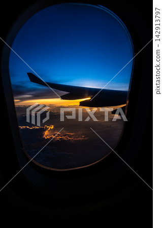 Breathtaking View from an Airplane Window at Sunset, Showcasing Wing Silhouette Against Vibrant Sky Colors and Clouds Below. Breathtaking View from an Airplane Window at Sunset, Showcasing Wing Silhouette Against Vibrant Sky Colors and Clouds Below. 142913797