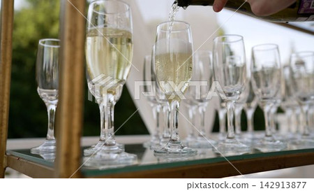 Hand pouring sparkling wine into elegant flute glasses on tray for celebration 142913877