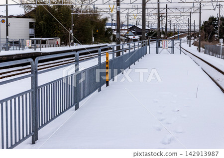 通往被雪覆蓋的無人值守車站月台的腳印;冬季本地列車站台;低角度拍攝。 通往被雪覆蓋的無人值守車站月台的腳印;冬季本地列車站台;低角度拍攝。 142913987