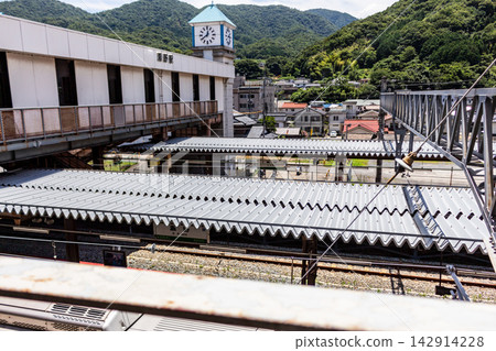 A local train station platform with a clock tower, a mountain townscape, and an aerial view from a high vantage point. A local train station platform with a clock tower, a mountain townscape, and an aerial view from a high vantage point. 142914228