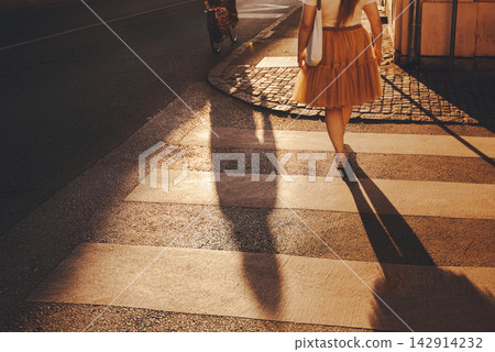 Woman Walking Across City Street at Sunset Woman Walking Across City Street at Sunset 142914232