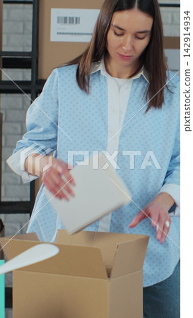 Vertical video. Female online store business owner, worker, packs books after e-commerce retail order delivery into box, prepares package delivery on table. Vertical video. Female online store business owner, worker, packs books after e-commerce retail order delivery into box, prepares package delivery on table. 142914934