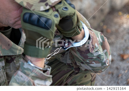 Close-up of handcuffed military hands representing counterintelligence, espionage, arrest, investigation and security concepts. Close-up of handcuffed military hands representing counterintelligence, espionage, arrest, investigation and security concepts. 142915164