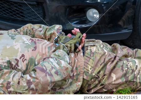 Man in military camouflage lies on the ground beside a vehicle with his hands restrained in handcuffs. Man in military camouflage lies on the ground beside a vehicle with his hands restrained in handcuffs. 142915165