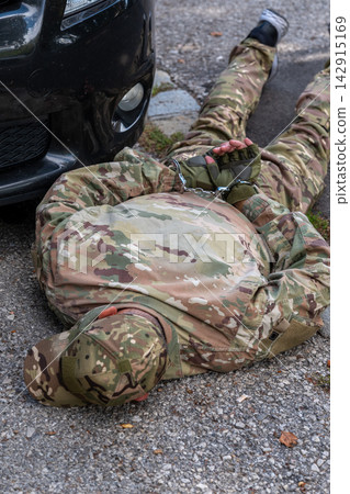Man in military camouflage lies handcuffed beside a vehicle following a simulated security service arrest. Man in military camouflage lies handcuffed beside a vehicle following a simulated security service arrest. 142915169