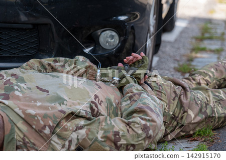 Soldier in camouflage uniform lies beside a car with his hands restrained in handcuffs after detention. 142915170
