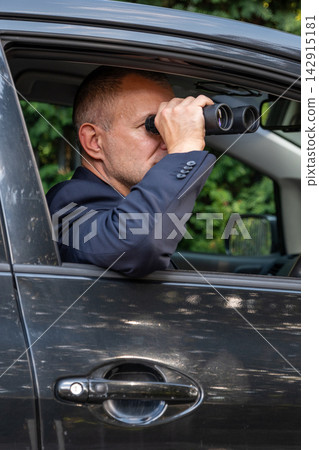 Intelligence agent conducting covert surveillance with binoculars Intelligence agent conducting covert surveillance with binoculars 142915181