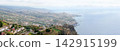 Panoramic coastal landscape with hillside houses, terraced farmland, rugged cliffs, and ocean under a cloudy sky on Madeira Island, Portugal 142915199