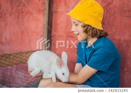 Happy child holds a white rabbit during an educational animal encounter. Joy and connection during a farm animal encounter. Happy child holds a white rabbit during an educational animal encounter. Joy and connection during a farm animal encounter. 142915245